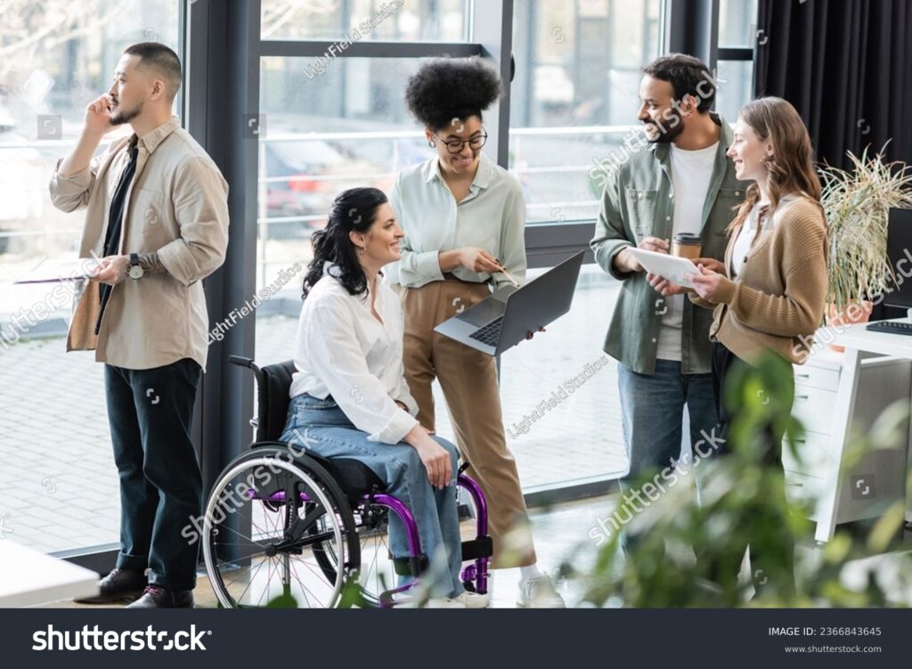 stockphotocheerfulinterracialbusinesspeopleanddisabledwomaninwheelchairusingdevicesincoworking2366843645 iWorkZoom